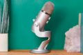  یک میکروفون USB Blue Yeti روی میز روی جلوی یک دیوار سبز در پس زمینه 